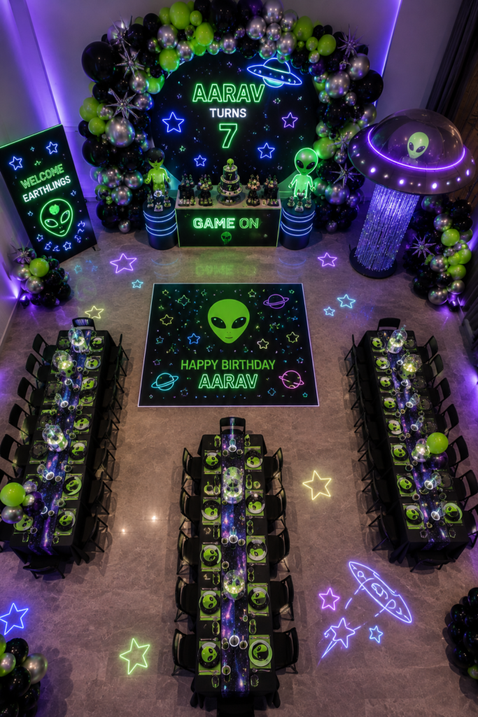 Alien and UFO–themed birthday party setup featuring neon green, purple, black, and silver decorations with glowing extraterrestrial graphics. A personalized backdrop reads 'Aarav Turns 7' and is framed by balloon garlands, illuminated stars, planets, and alien figures. The celebration includes a themed cake, galaxy-inspired dining tables, a large UFO prop, glowing floor projections, and a dance floor displaying 'Happy Birthday Aarav,' creating an immersive cosmic adventure atmosphere