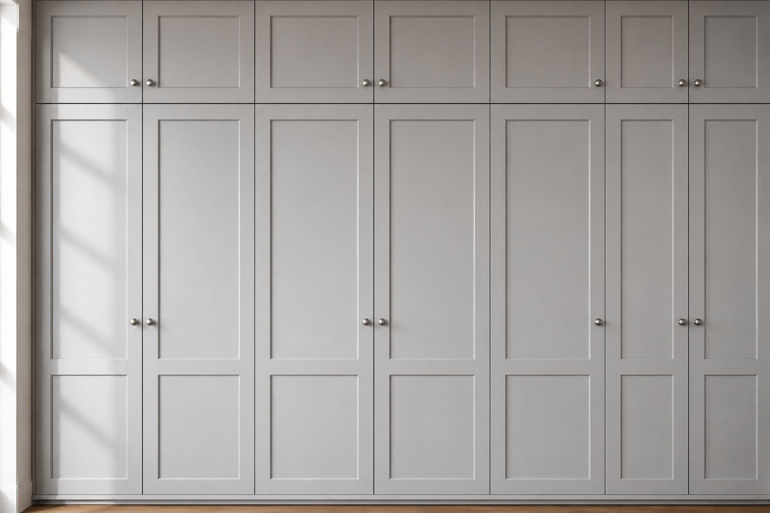 Wide view of floor-to-ceiling light grey shaker kitchen cabinets with a matte finish, brushed nickel knobs, subtle wood grain texture, and soft natural daylight in a modern kitchen.