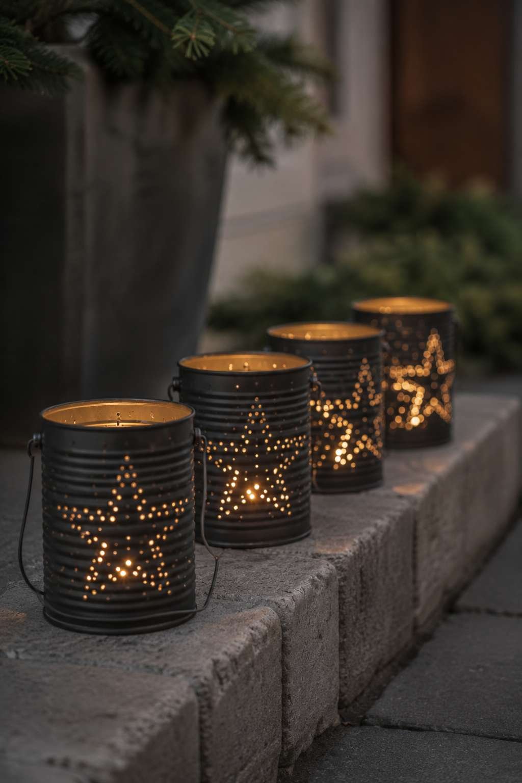 Four black metal star lanterns with glowing candles line a stone ledge outdoors at dusk, creating a warm and festive holiday display. 