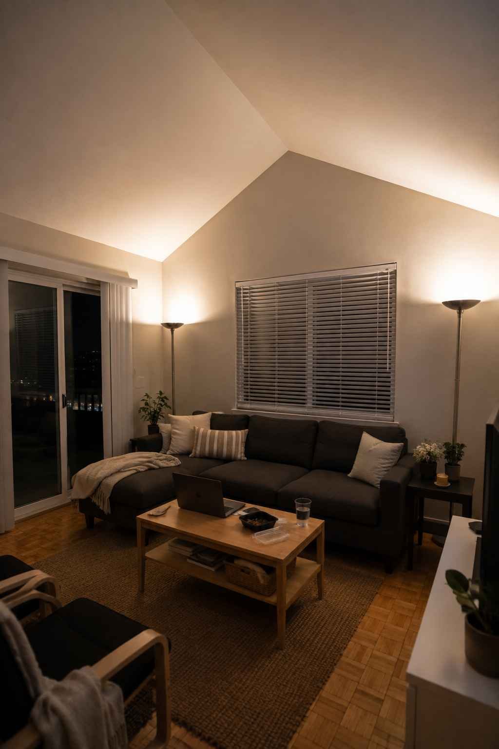 Small vaulted ceiling living room with soft uplighting, neutral furniture, and a warm, inviting evening atmosphere.