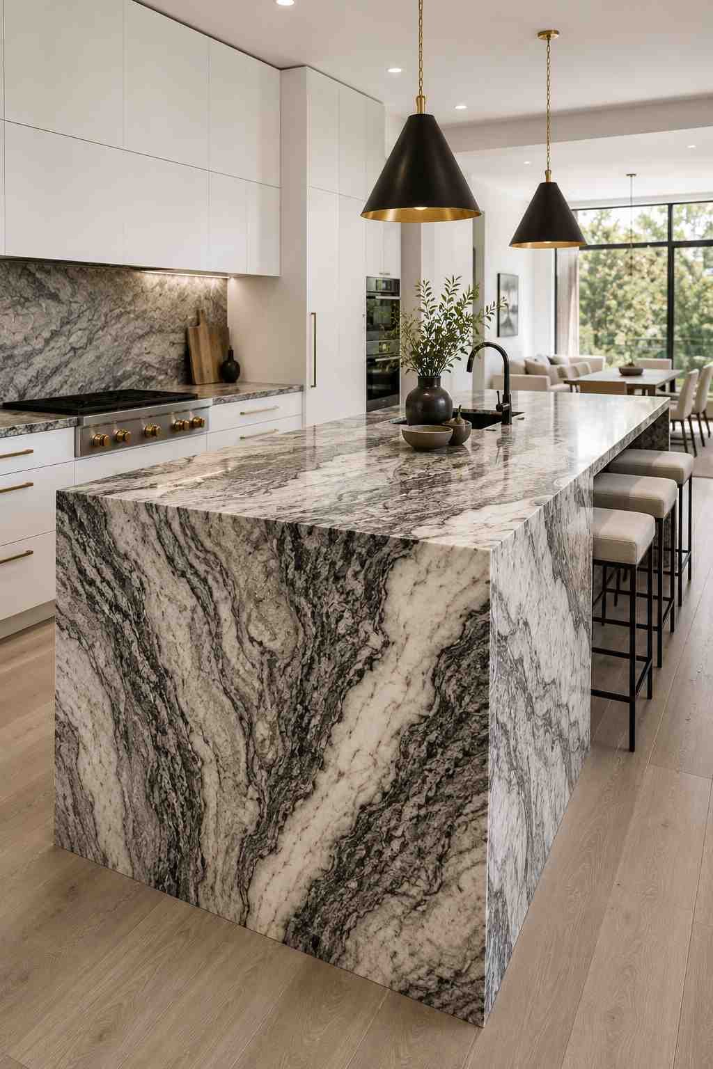 Modern kitchen featuring a dramatic waterfall granite island with continuous gray and white veining, white flat-panel cabinets, minimalist hardware, sculptural pendant lighting, light wood flooring, and an open-concept layout with contemporary styling.